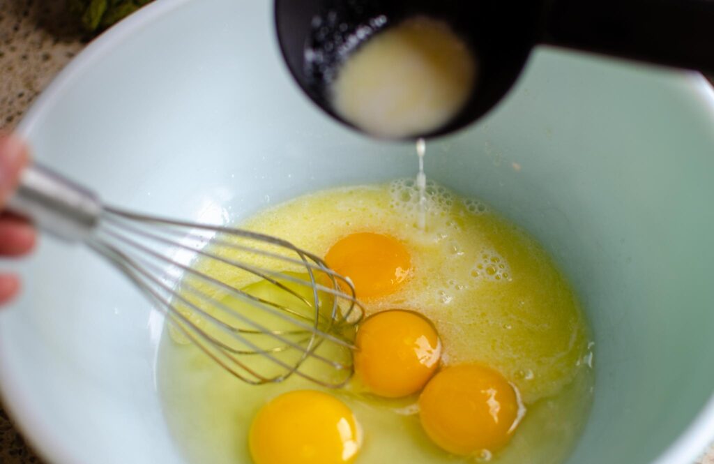 pouring milk mixture over eggs while whisking to temper the eggs