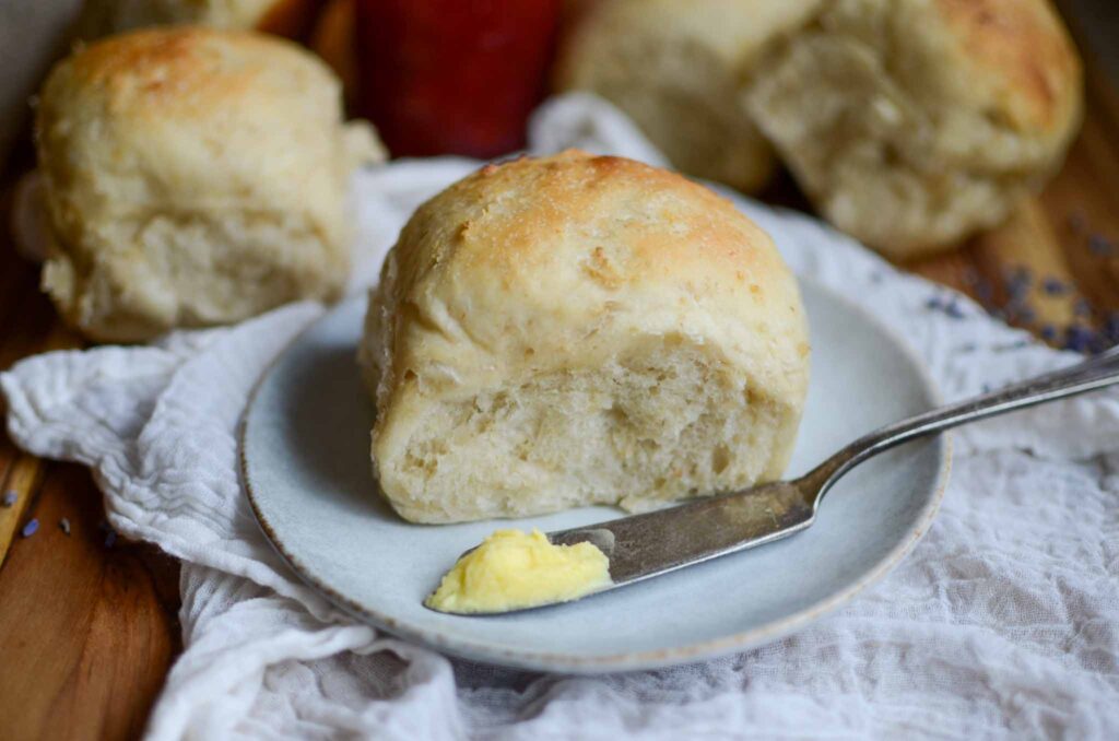 a sourdough oatmeal dinner roll on a plate with a knife full of butter.