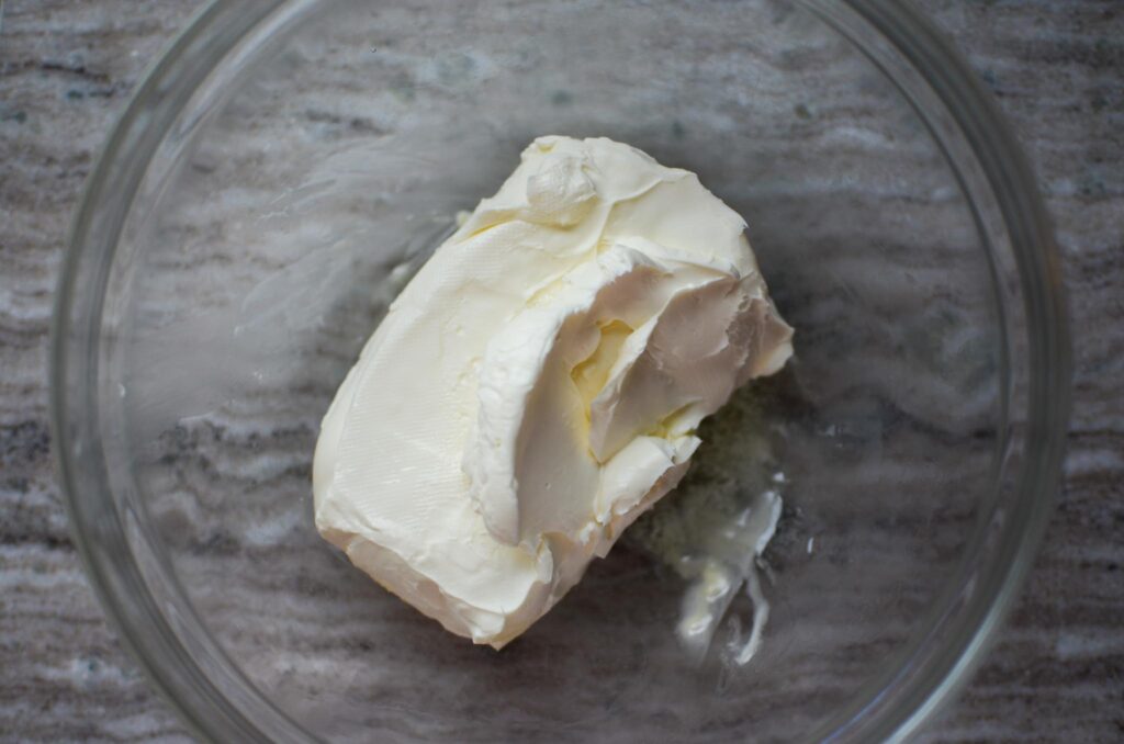 a brick of cream cheese in a glass mixing bowl