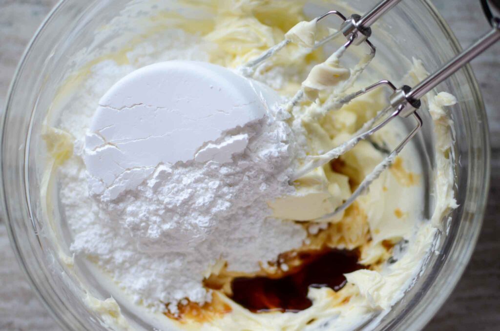 adding vanilla extract and confectioners' sugar to cream cheese and butter mixture