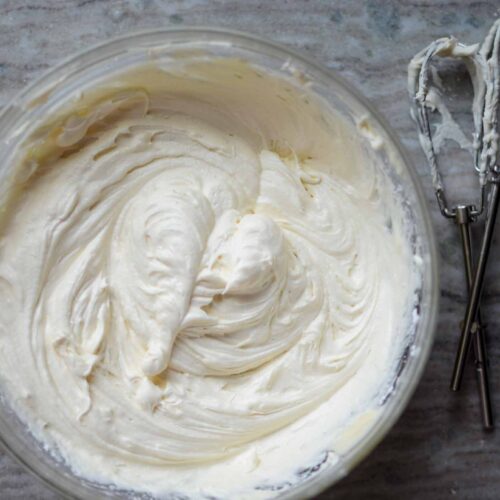 a bowl of homemade cream cheese frosting with beaters filled with frosting