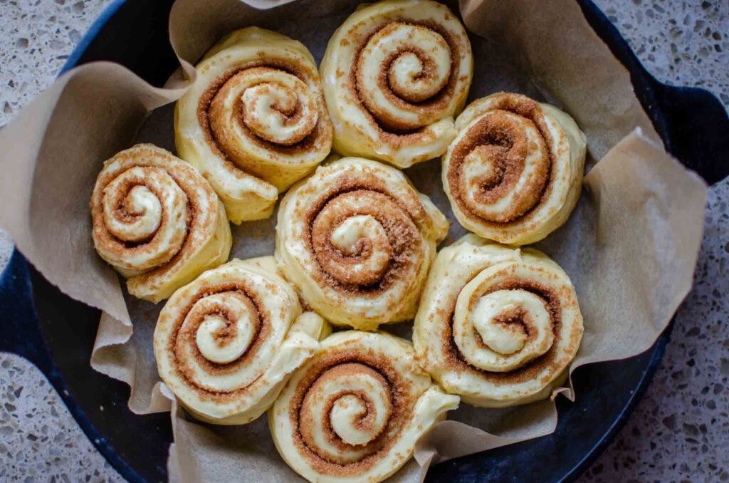 arranged rolled sourdough cinnamon rolls in parchment lined cast iron skillet