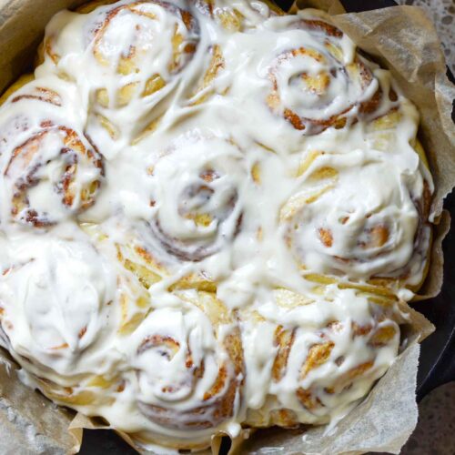 fluffy sourdough cinnamon rolls in cast iron round pan with parchment paper