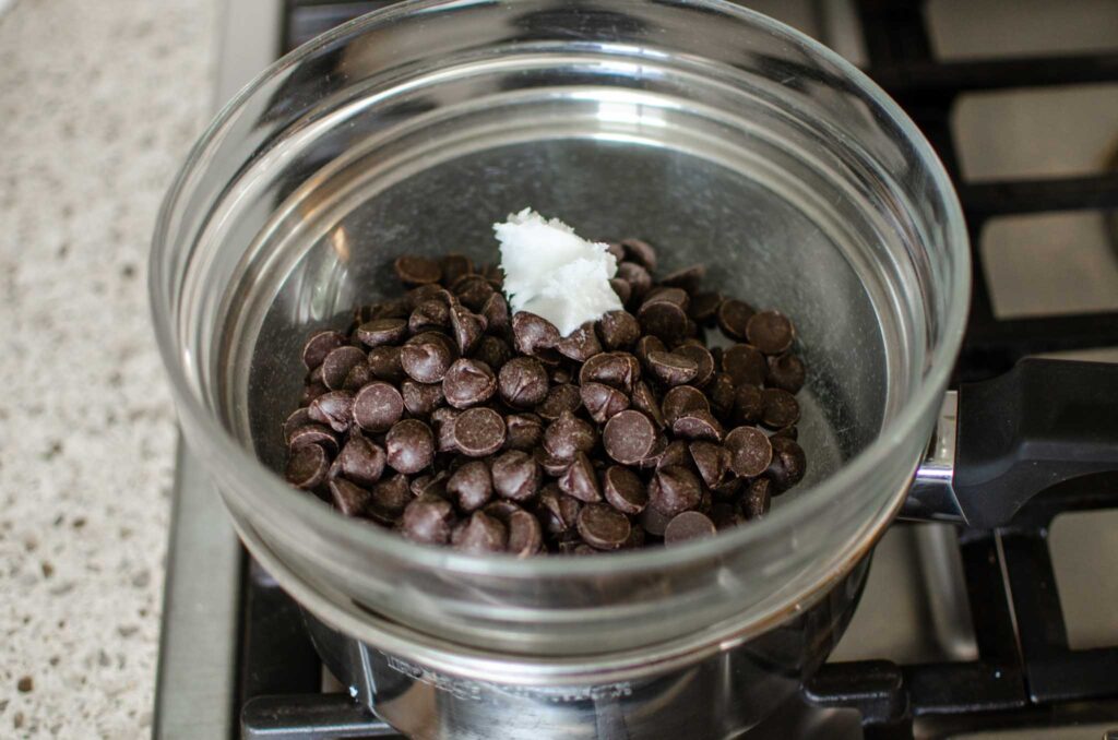 chocolate chips and coconut oil in glass bowl in double boiler