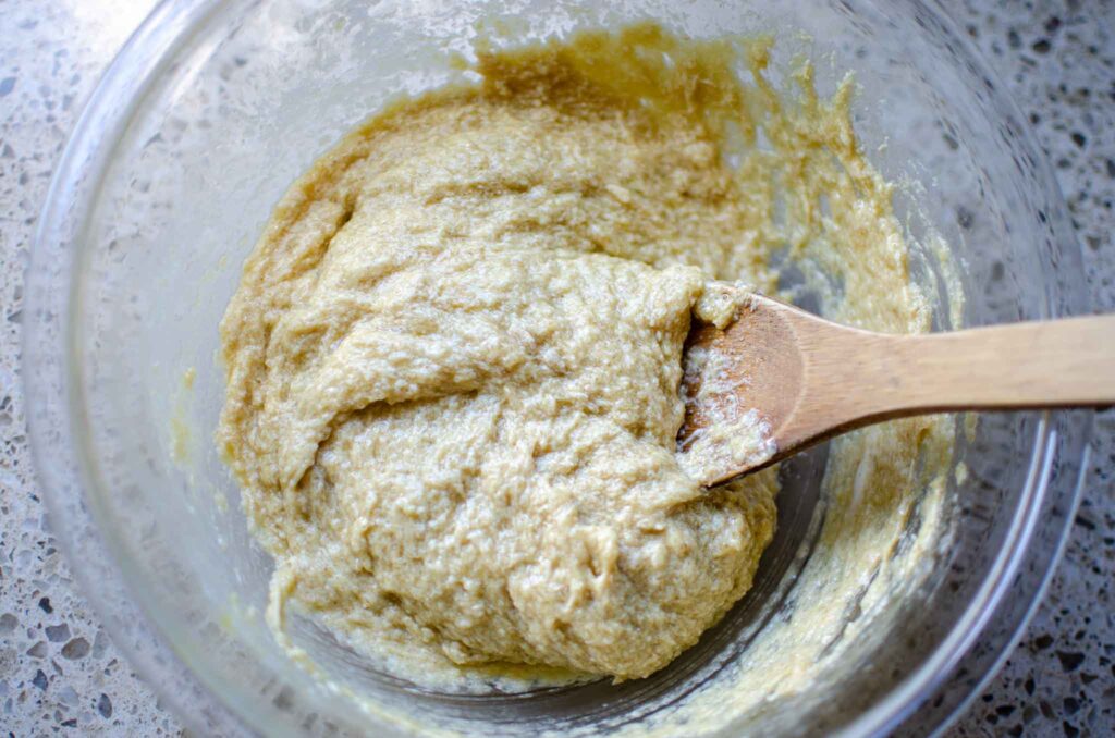 all of the wet ingredients combined in glass bowl with wooden spoon