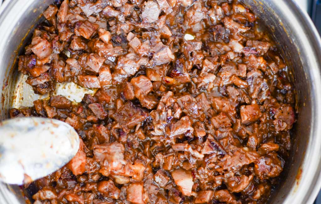 Heating up chopped beef brisket in bbq sauce in saucepan