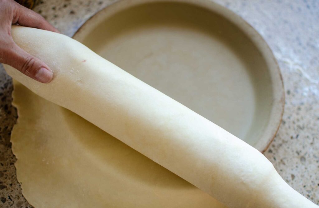 rolling out pie crust with rolling pin into pie pan