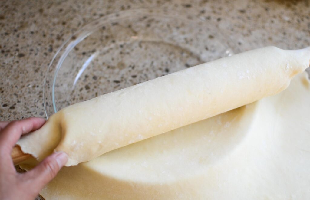 rolling sourdough pie crust off of the rolling pin onto the pie plate