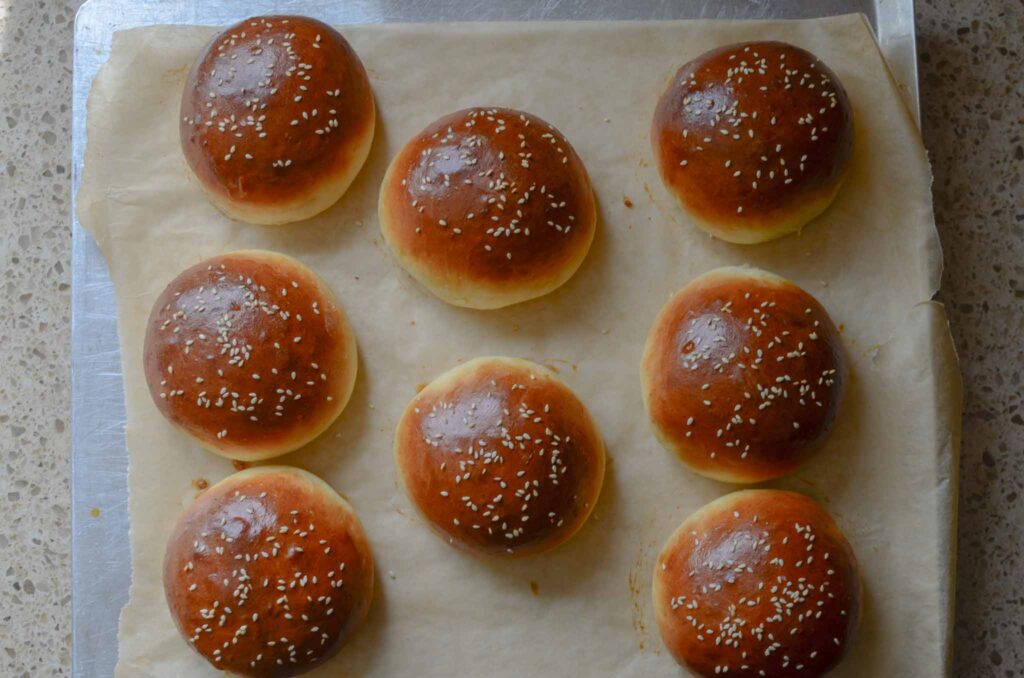 Golden baked homemade hamburger buns on baking sheet