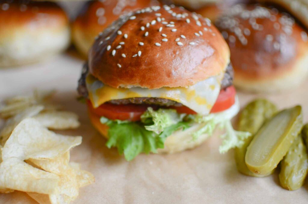 hamburger with fixings, pickles, and chips on the side.