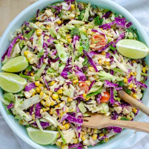 Mexican street corn salad in large bowl with lime wedges.