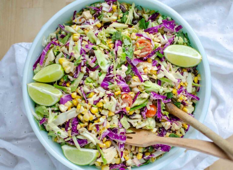 Mexican street corn salad in large bowl with lime wedges.