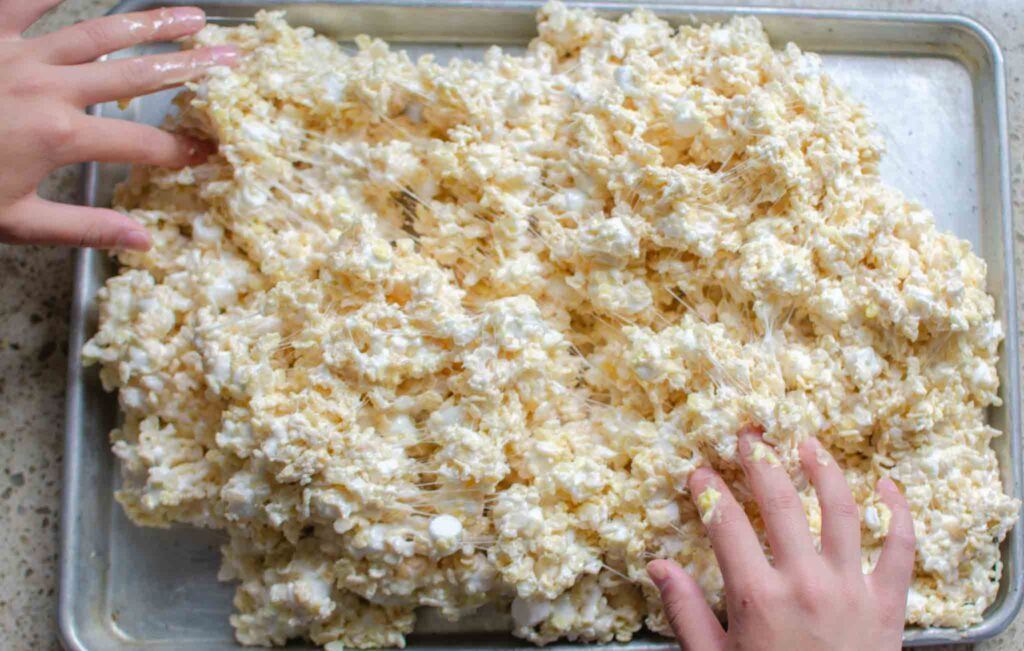 spreading rice krispies and marshmallow mixture out into large pan