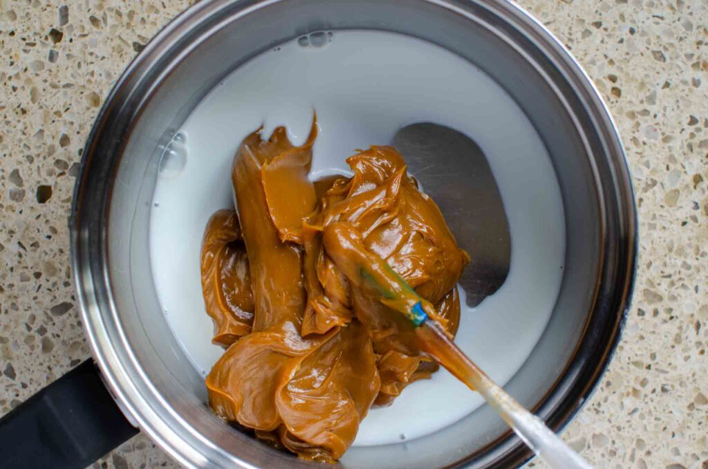 dulce de leche and milk in sauce pan with rubber spatual