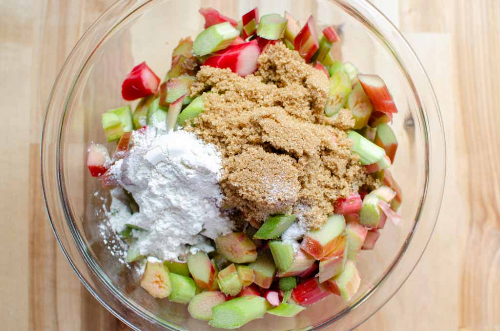 adding brown sugar, flour, salt and vanilla extract to rhubarb in glass bowl