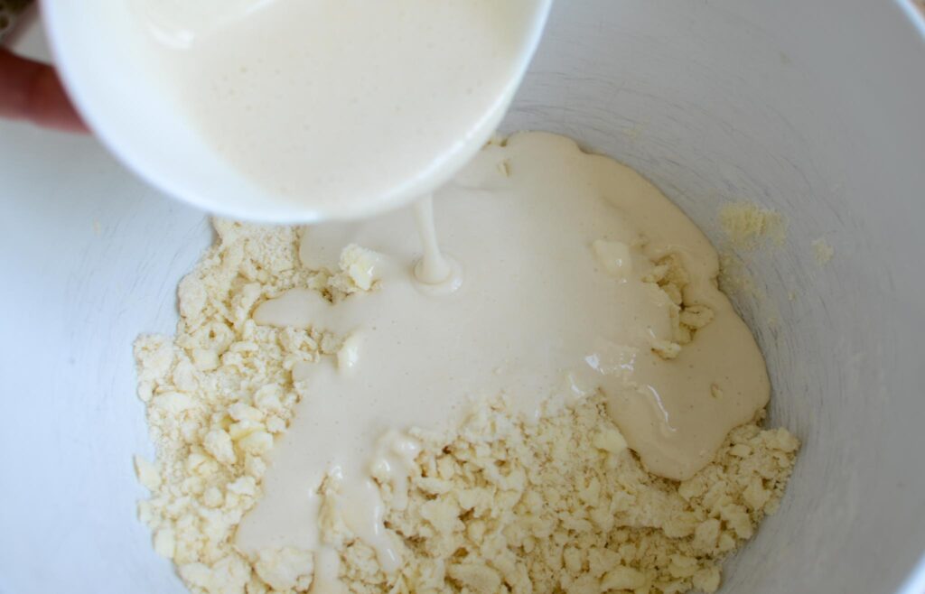 Pouring wet ingredients over dry ingredients in white bowl for sourdough pie crust