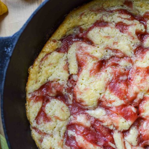 Rhubarb spoon cake in a cast iron skillet with rhubarb stalks and cut lemon