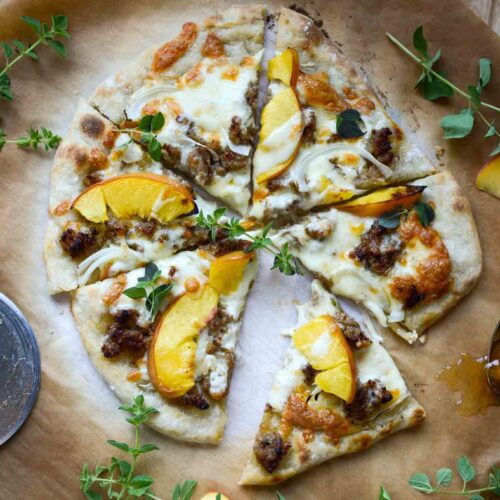 Italian sausage and peach pizza cut into slices on parchment paper