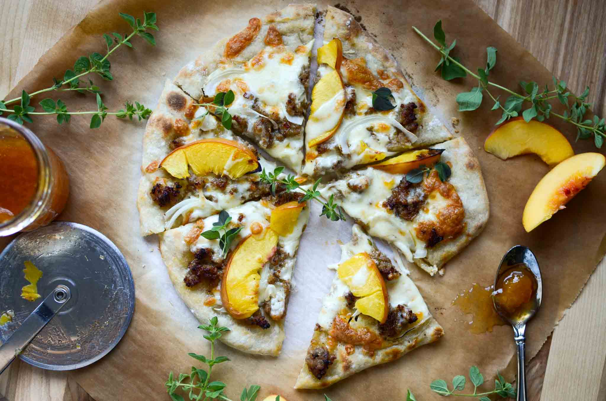 Italian sausage and peach pizza cut into slices on parchment paper