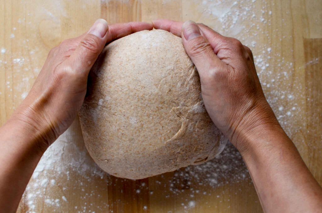 pulling the bread towards yourself to create a round dough shape