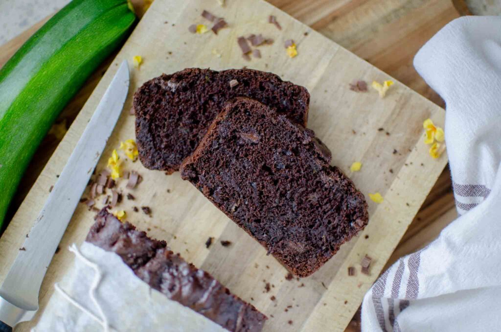 sourdough chocolate zucchini bread slices on wooden cutting board with knife and whole zucchini