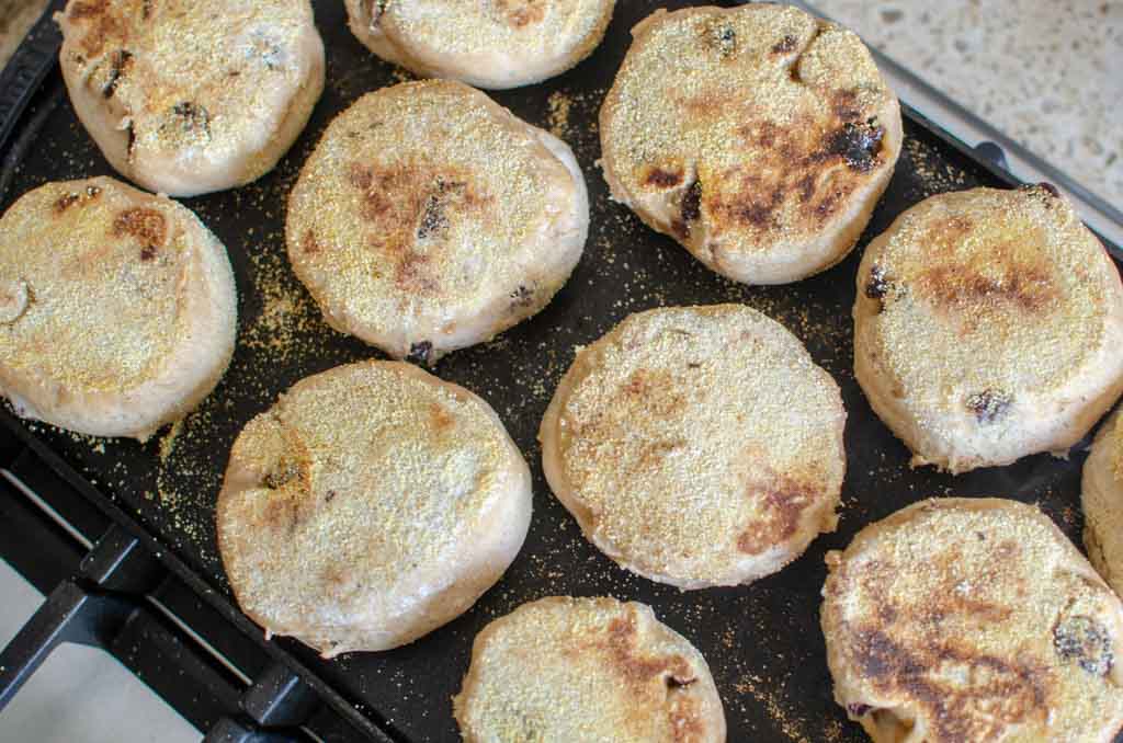 many sourdough English muffins cooking on cast iron griddle 