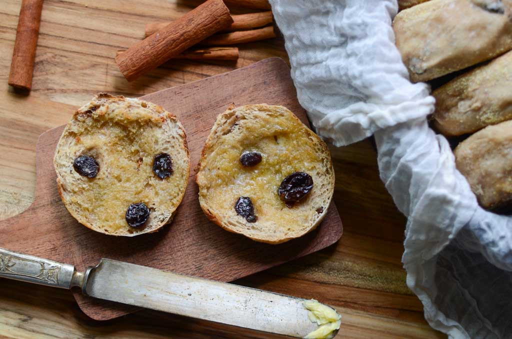 Sourdough cinnamon raisin English muffin sliced in half with cinnamon sticks and butter knife.