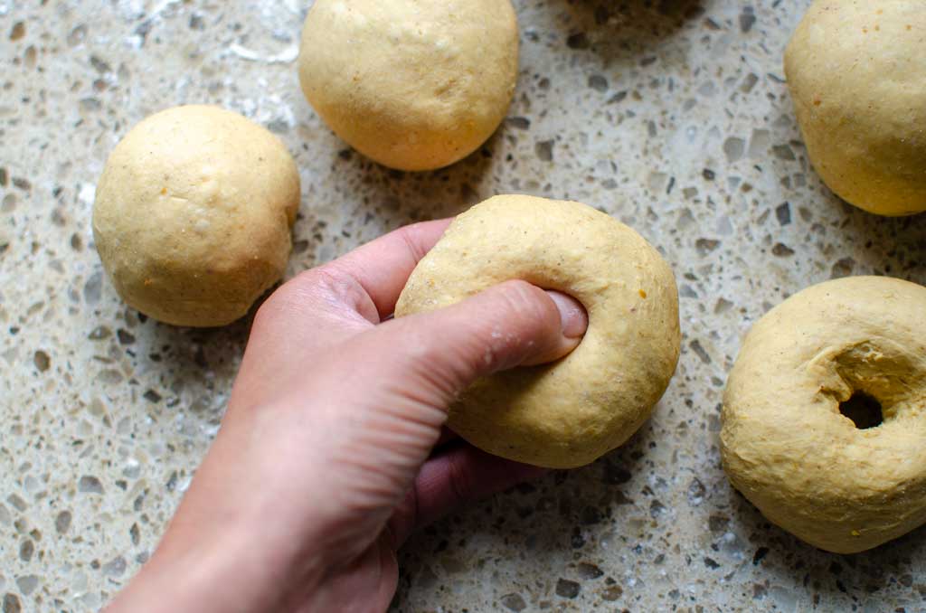 pushing thumb and finger in the middle of the ball of dough to form the hole of a bagel