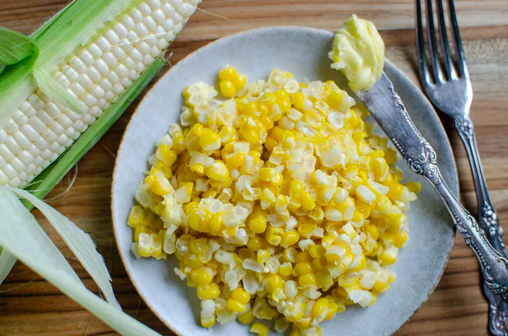 a plate of sweet corn kernels with a corn cob next to the plate