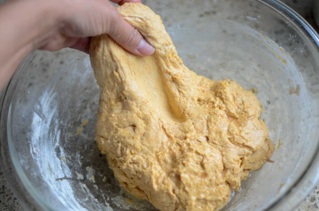 Stretching the sourdough pumpkin dough straight up in a glass bowl