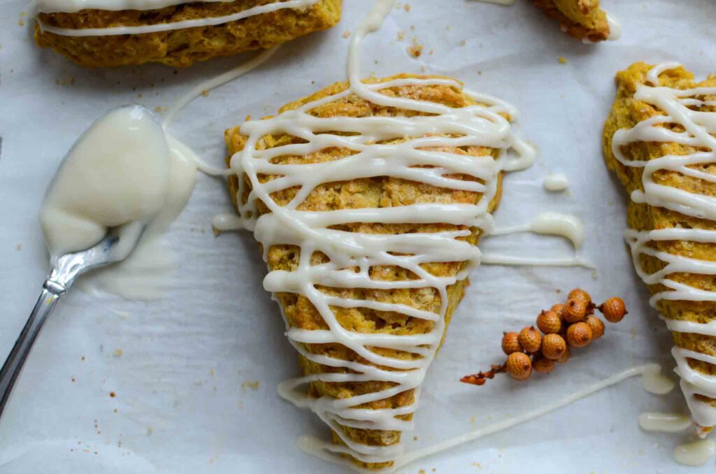 sourdough pumpkin scones with cream cheese glaze on a parchment-lined baking sheet with a spoonful of glaze.