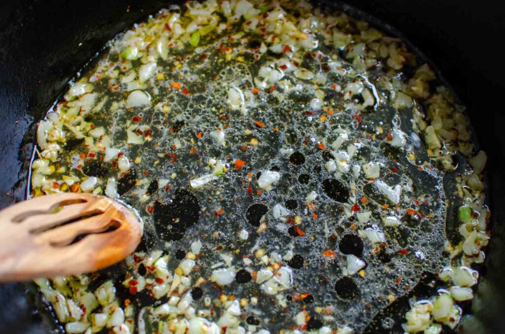 oil, minced garlic, and red pepper flakes in a pan with a wooden spoon. 