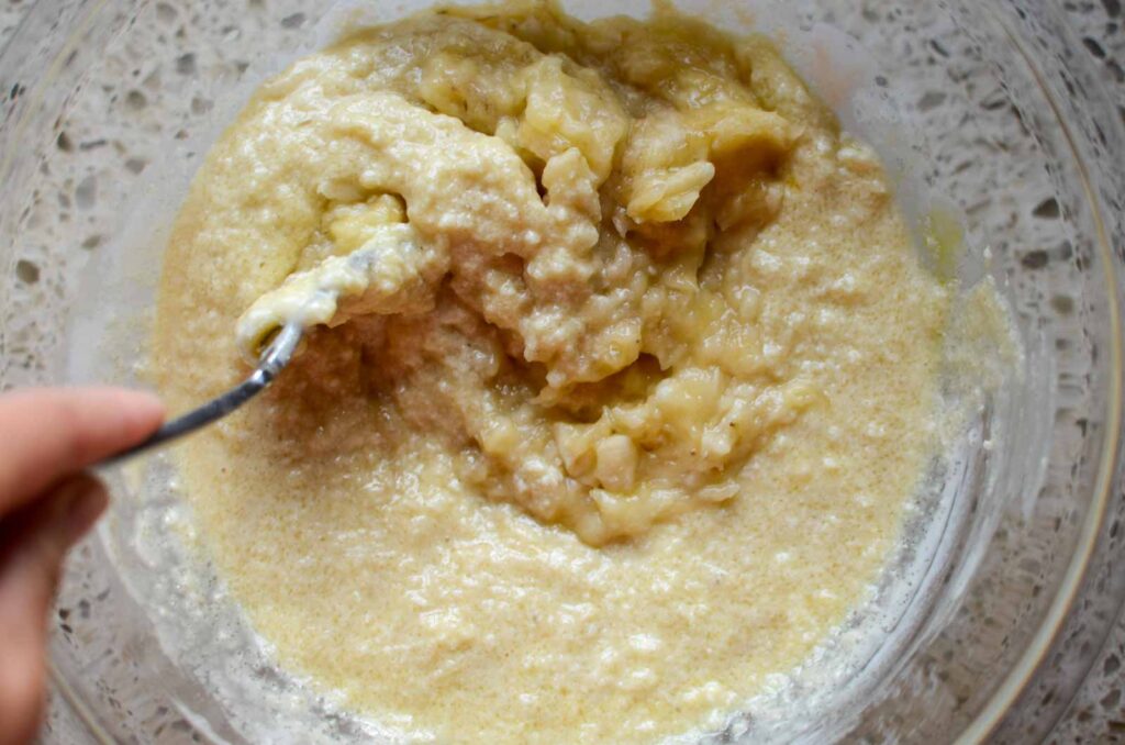 Adding mashed banana to wet ingredients in glass bowl