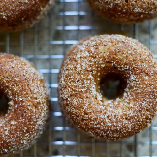 cinnamon and sugar-covered sourdough apple cider donuts on wire rack