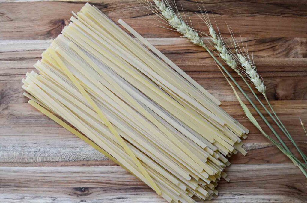 dried pasta on a wood cutting board with a few stalks of wheat