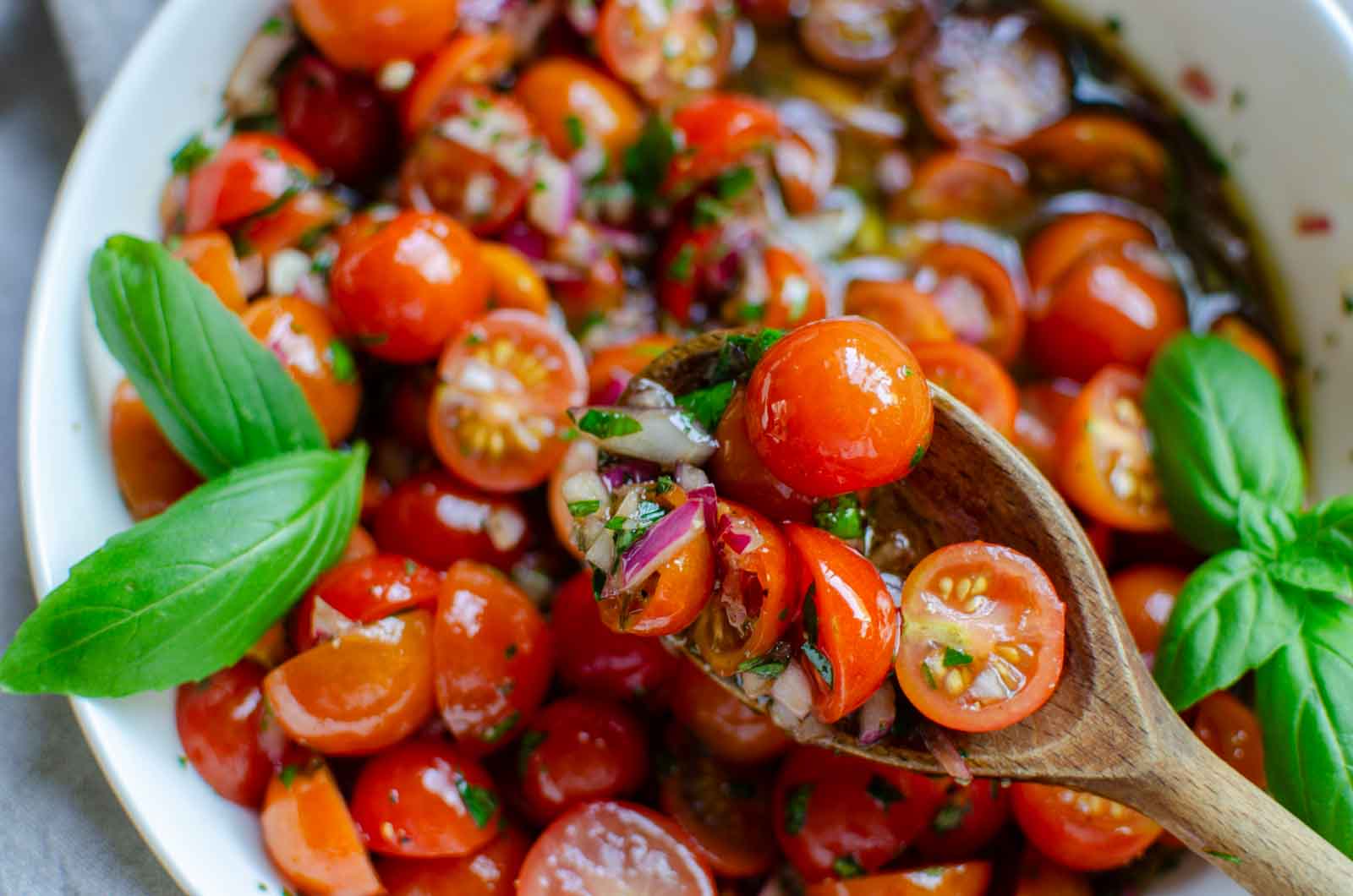 marinated tomatoes served with a wooden spoon.