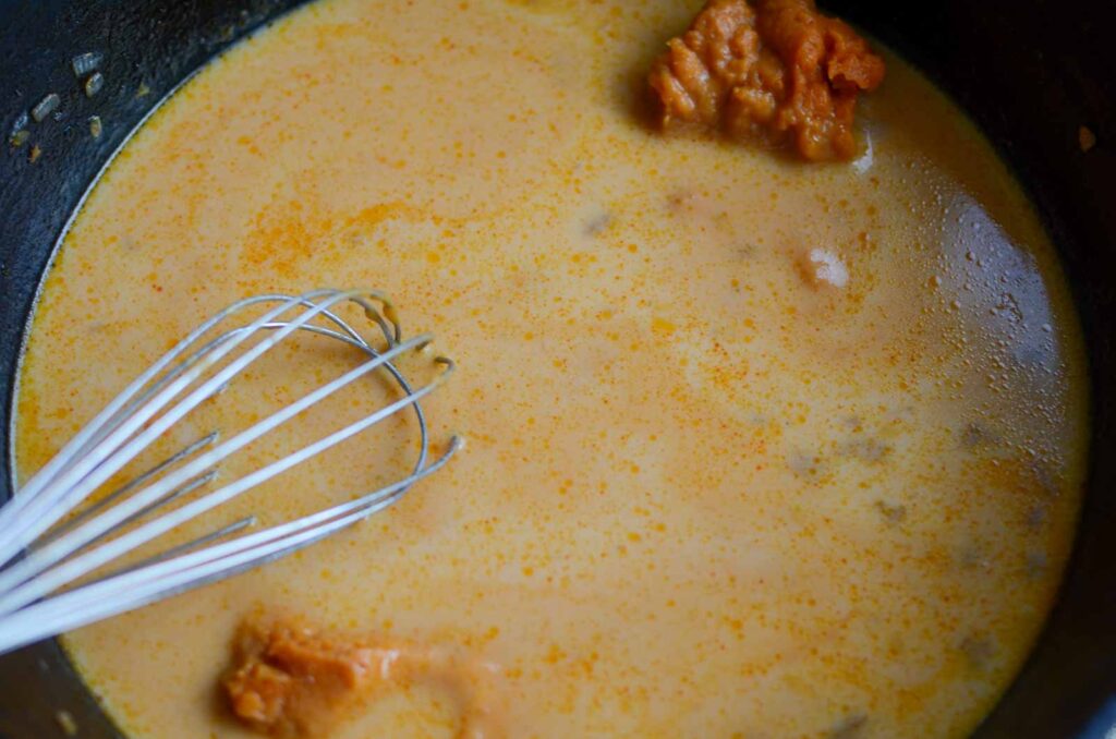 whisking pureed pumpkin, milk, and chicken stock in a pan