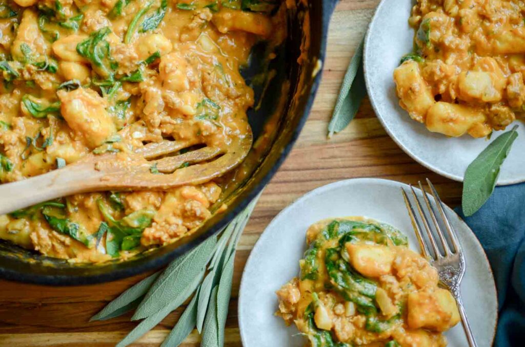 Pumpkin gnocchi with sausage and spinach in a skillet and small plates.