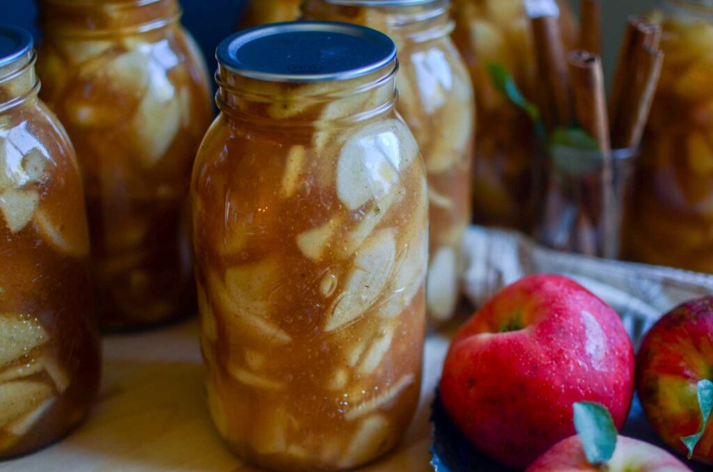 jars of pie filling with red apples and cinnamon sticks