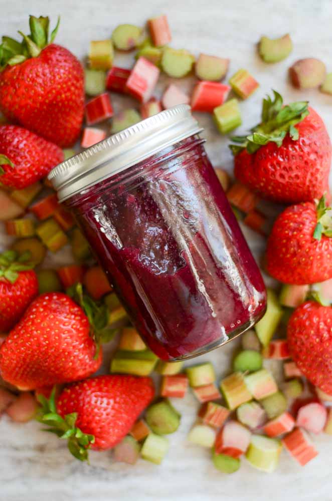 mixed berry jam in jar among berries and cut up rhubarb