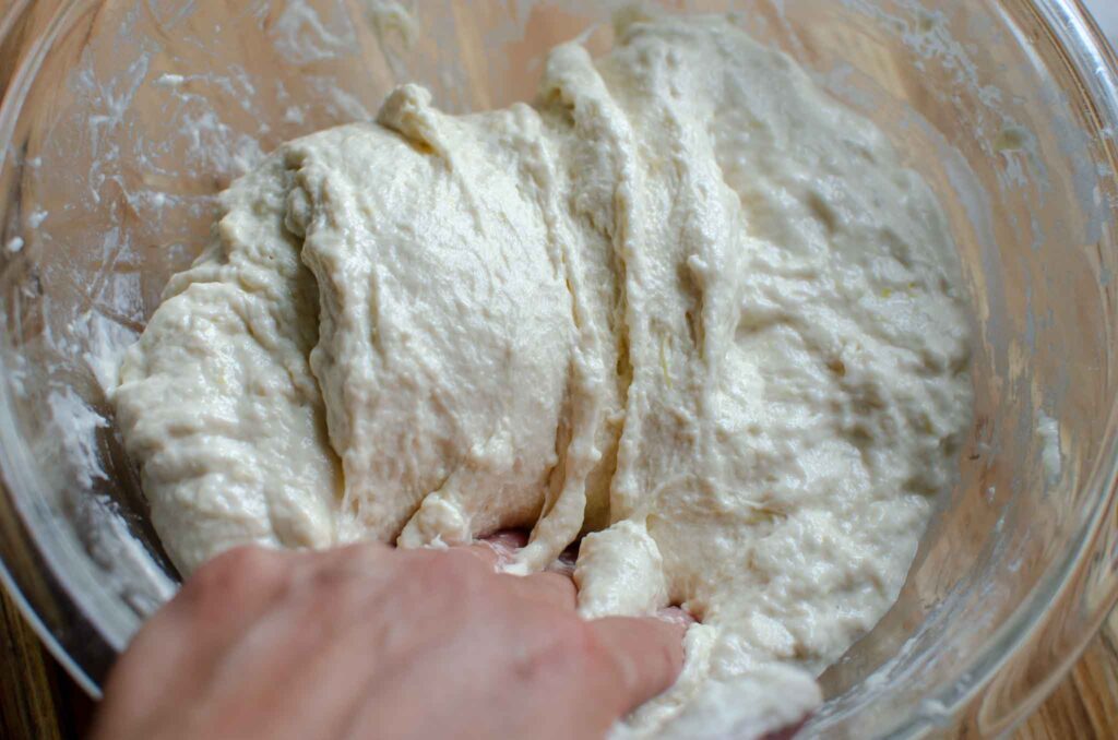 folding sourdough lemon focaccia dough in glass bowl