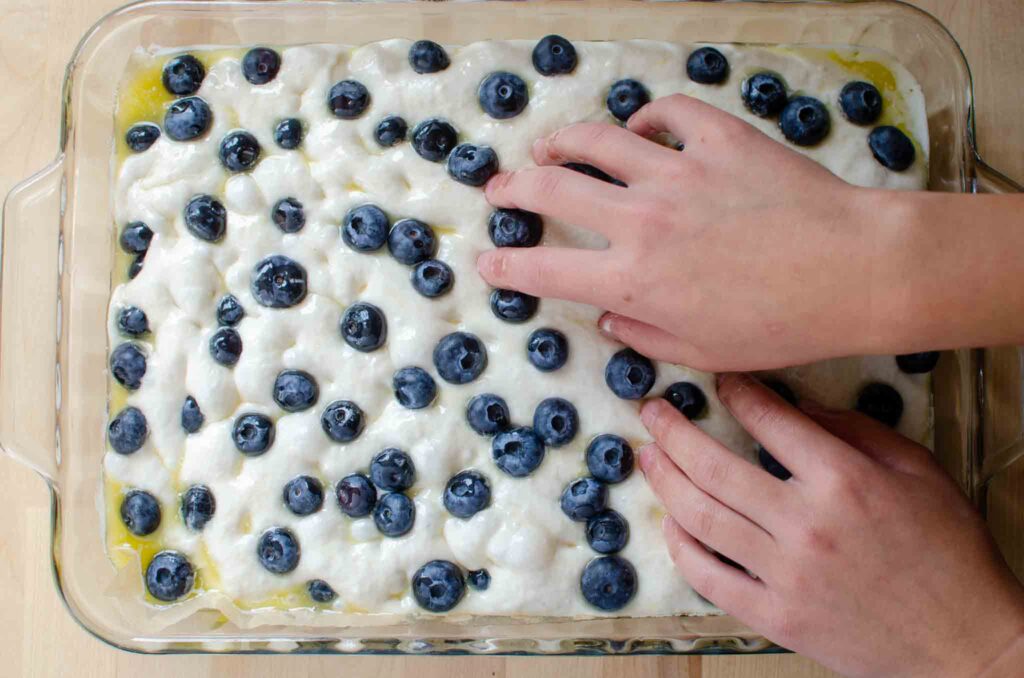 pressing dimples into sourdough focaccia bread dough with blueberries