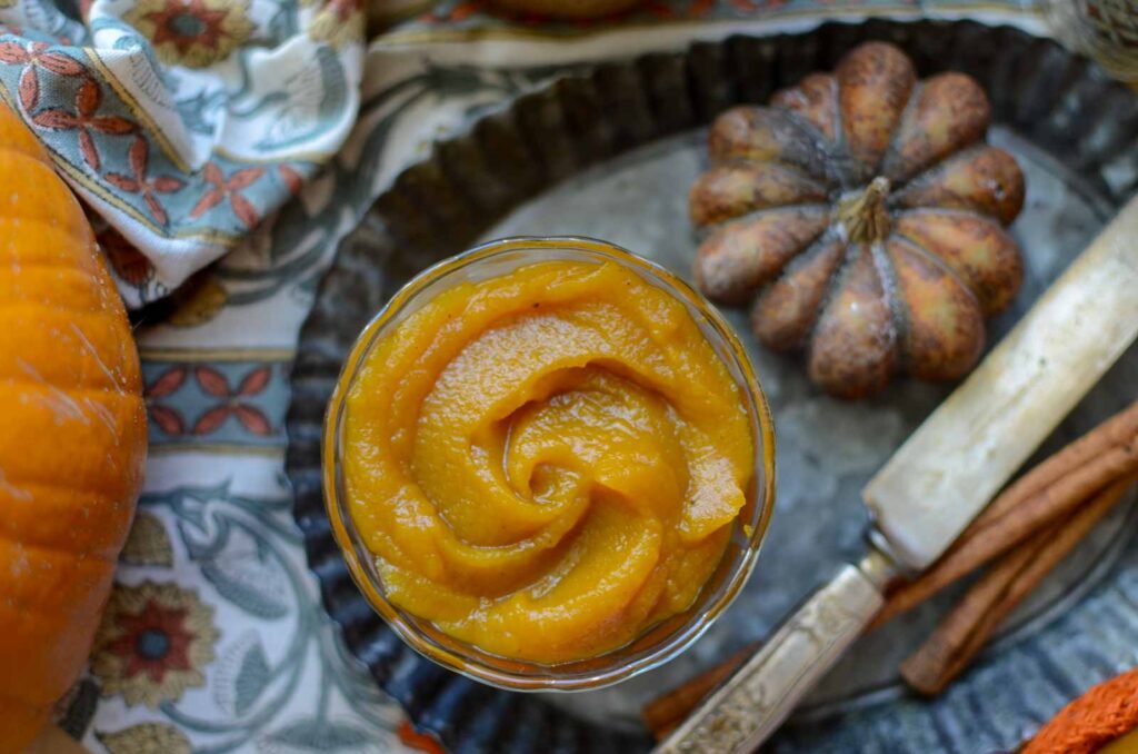 Homemade maple bourbon pumpkin butter in a small bowl next to a decorative pumpkin and knife