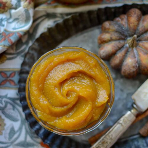 Homemade maple bourbon pumpkin butter in a small bowl next to a decorative pumpkin and knife