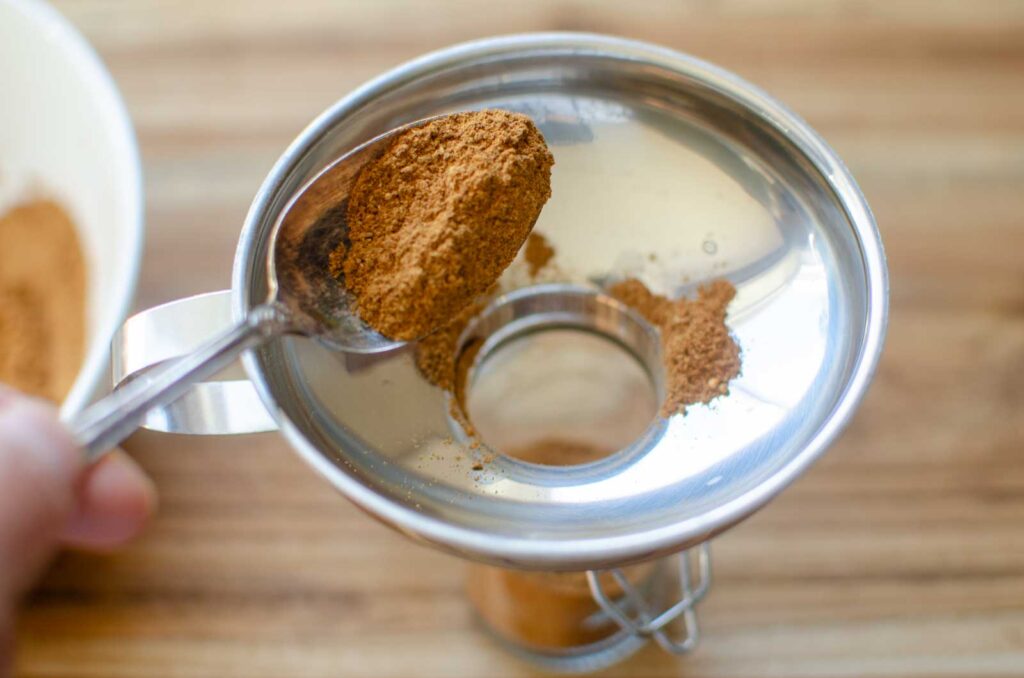 spooning spice blend into a small spice jar fitted with a funnel