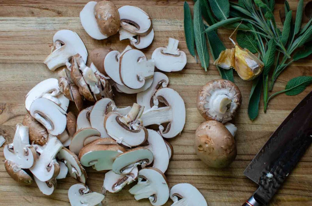 sliced mushrooms and sage leaves on cutting board