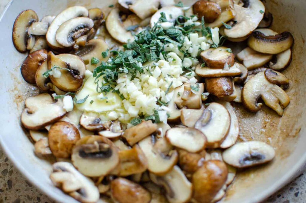 adding minced garlic cloves and sage to mushrooms in frying pan