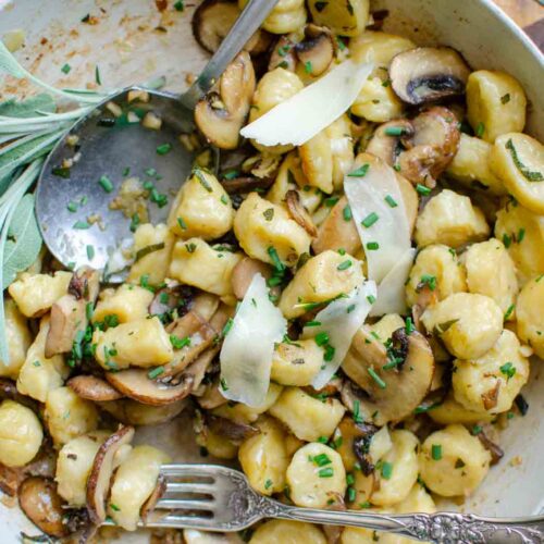 ricotta gnocchi with mushrooms and sage garlic butter sauce in large fry pan. A bundle of sage off to the side.