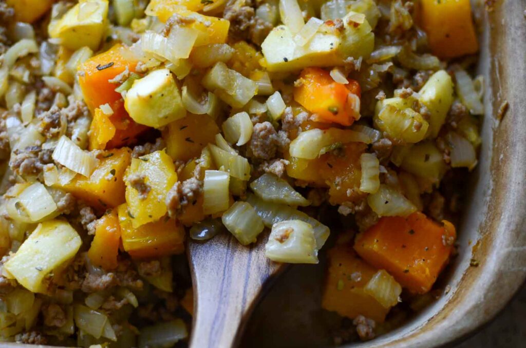 Wooden spoon lifting butternut squash casserole in stoneware