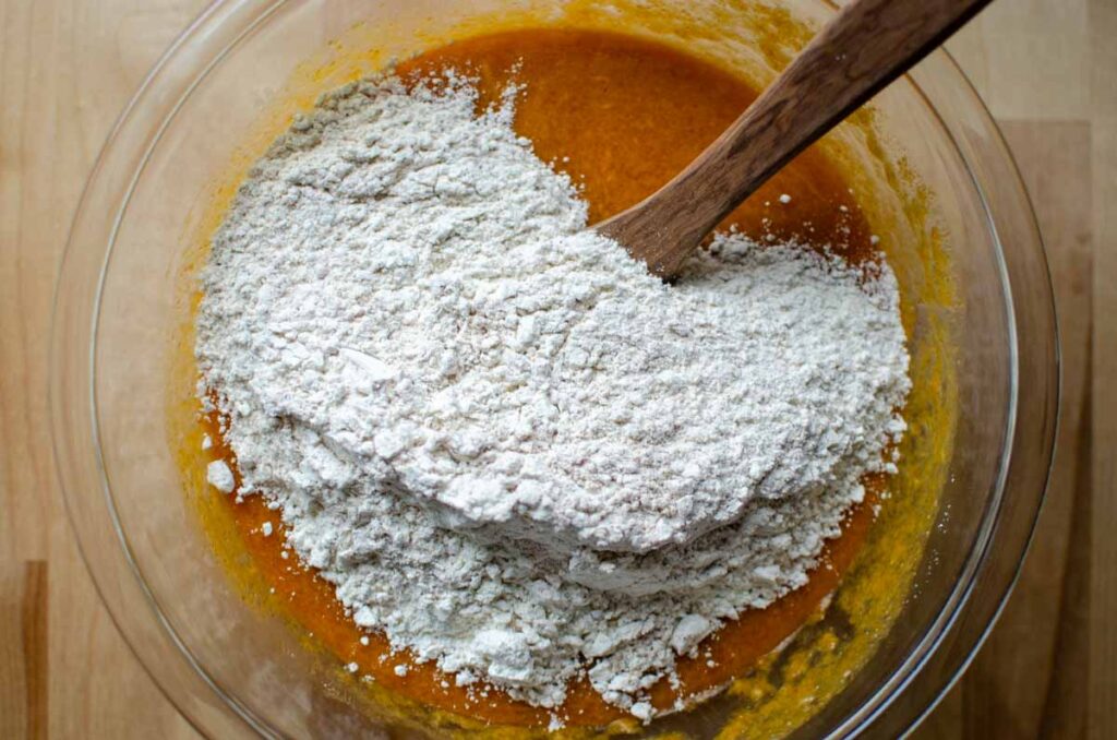 adding dry ingredients to wet ingredients in a glass bowl